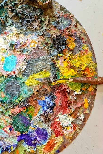 Vibrant close-up of a messy artist's palette covered in colorful paint with a mixing knife.